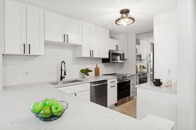 kitchen featuring sink, white cabinetry, stainless steel appliances, light stone counters, and decorative light fixtures