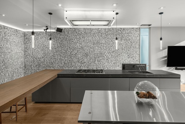 kitchen with tasteful backsplash, hanging light fixtures, light hardwood / wood-style floors, and stainless steel gas stovetop