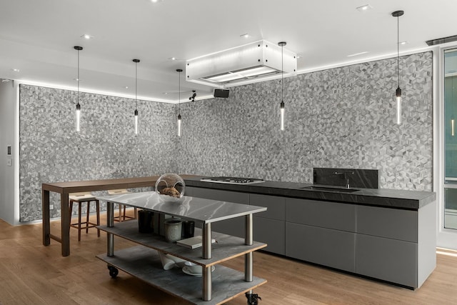 kitchen with gray cabinetry, pendant lighting, light hardwood / wood-style floors, and stainless steel gas cooktop