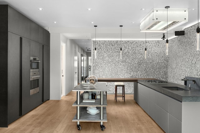 kitchen featuring sink, gray cabinetry, light wood-type flooring, appliances with stainless steel finishes, and pendant lighting