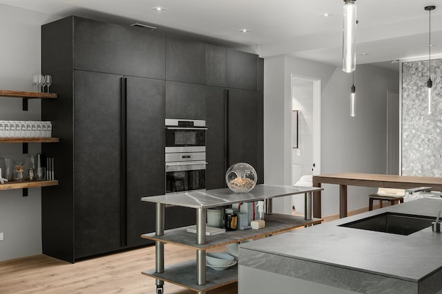 kitchen with double oven, hanging light fixtures, and light wood-type flooring