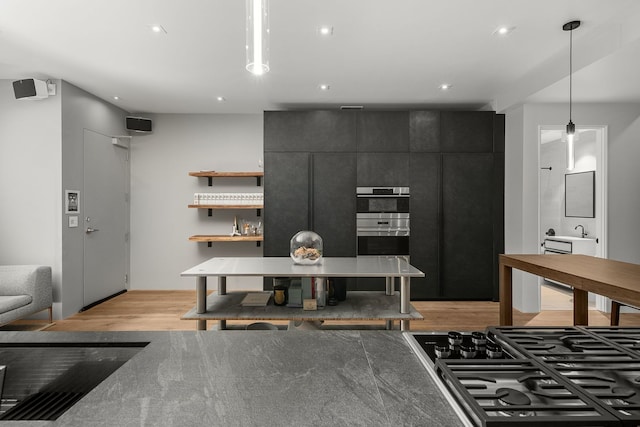 kitchen with hanging light fixtures, stovetop, double oven, and light hardwood / wood-style flooring