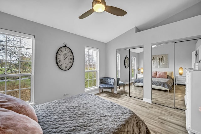 bedroom with ceiling fan, light hardwood / wood-style floors, vaulted ceiling, and two closets