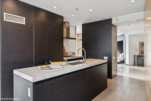 kitchen with sink, light tile patterned floors, an island with sink, and wall chimney exhaust hood