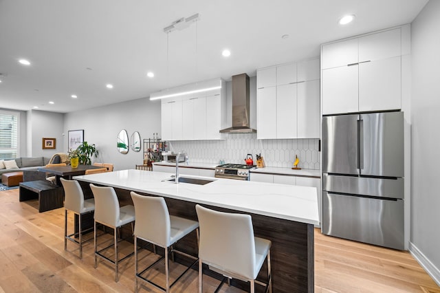 kitchen with a kitchen island with sink, wall chimney range hood, stainless steel appliances, and a kitchen breakfast bar