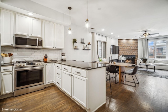 kitchen with dark wood-type flooring, stainless steel appliances, white cabinets, decorative light fixtures, and kitchen peninsula