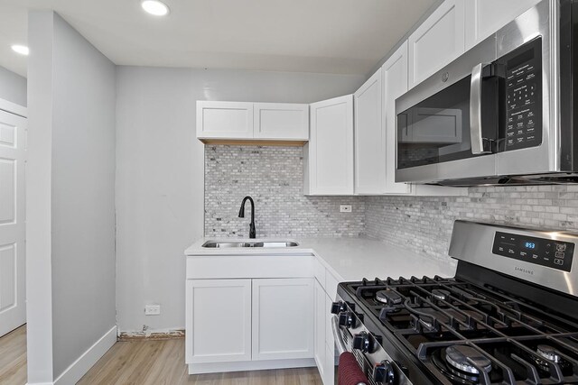 kitchen featuring white cabinetry, sink, decorative backsplash, light hardwood / wood-style floors, and stainless steel appliances