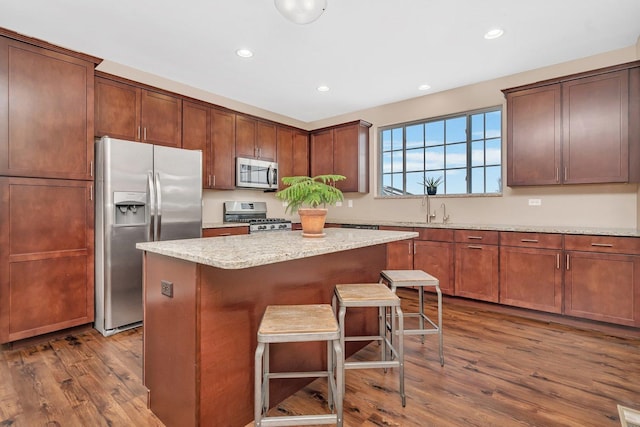 kitchen featuring a kitchen island, appliances with stainless steel finishes, dark hardwood / wood-style floors, a breakfast bar area, and light stone countertops