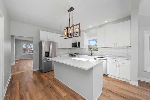 kitchen featuring hardwood / wood-style flooring, stainless steel appliances, a center island, white cabinets, and decorative light fixtures