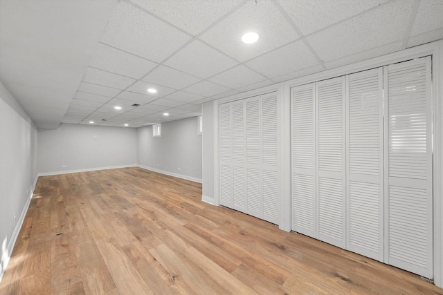 basement with a drop ceiling and light hardwood / wood-style flooring