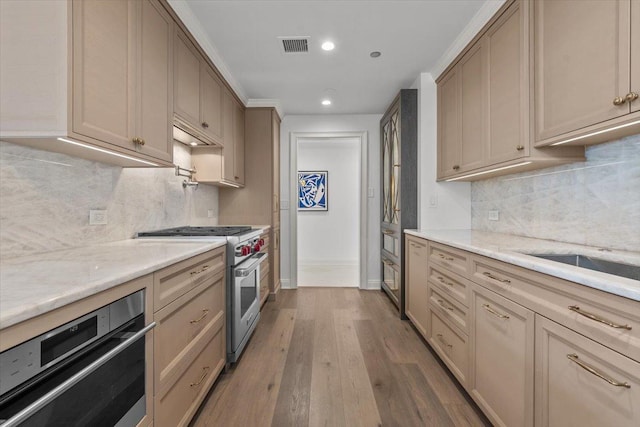 kitchen featuring stainless steel stove, hardwood / wood-style floors, light stone counters, decorative backsplash, and oven