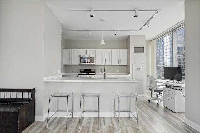 kitchen featuring appliances with stainless steel finishes, a breakfast bar, white cabinets, kitchen peninsula, and light wood-type flooring