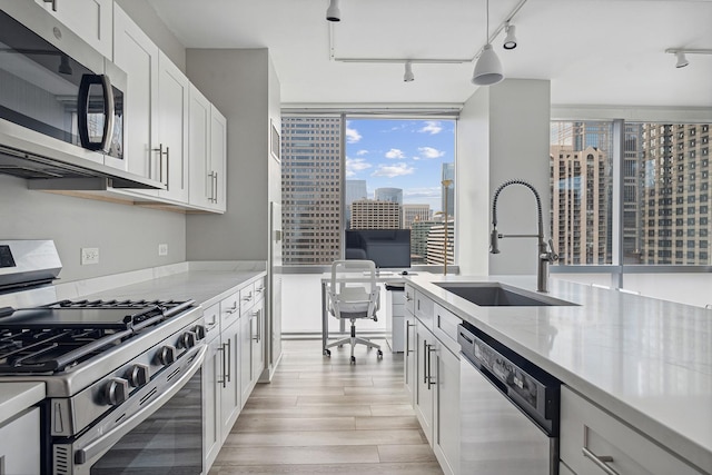 kitchen with appliances with stainless steel finishes, pendant lighting, white cabinetry, sink, and light wood-type flooring