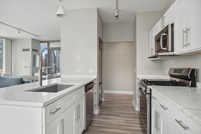 kitchen with sink, white cabinets, hanging light fixtures, stainless steel appliances, and light wood-type flooring