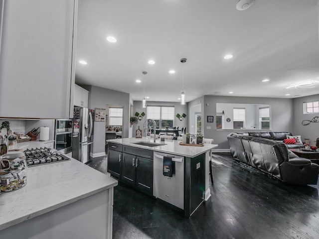 kitchen featuring appliances with stainless steel finishes, sink, white cabinets, hanging light fixtures, and a kitchen island with sink