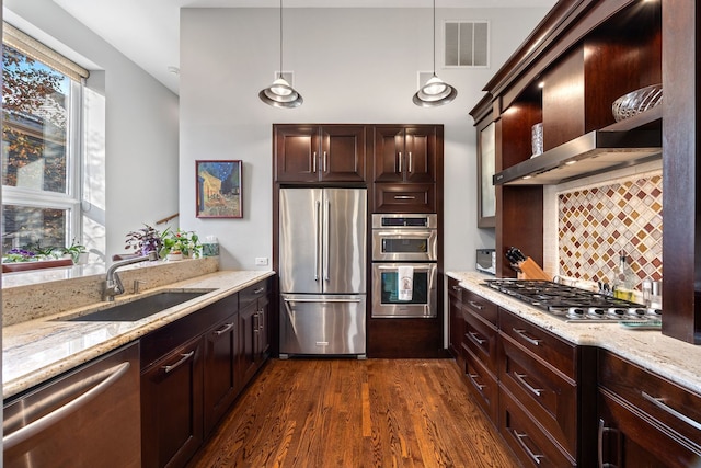 kitchen featuring sink, wall chimney range hood, appliances with stainless steel finishes, dark hardwood / wood-style floors, and decorative light fixtures