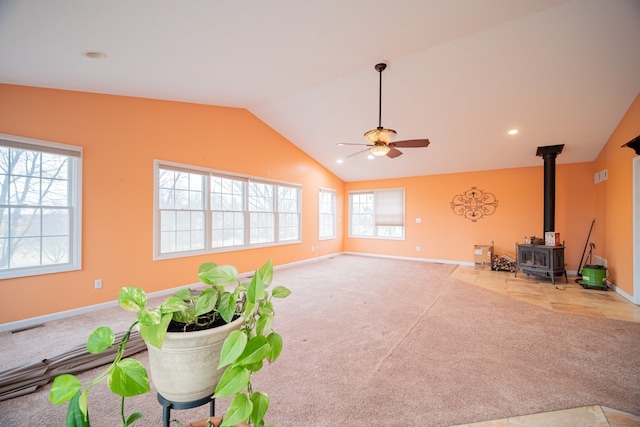 living room featuring ceiling fan, light colored carpet, vaulted ceiling, and a wood stove