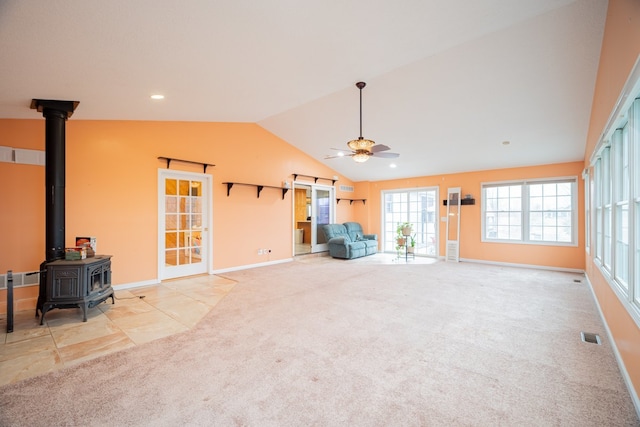 unfurnished living room featuring light carpet, vaulted ceiling, ceiling fan, and a wood stove