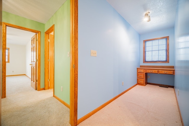 hallway featuring light colored carpet and a textured ceiling