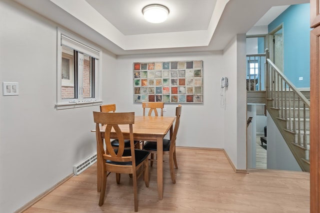 dining space featuring a raised ceiling, baseboard heating, and light wood-type flooring