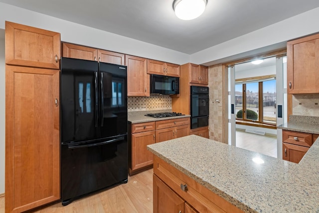 kitchen with light stone countertops, backsplash, black appliances, and light hardwood / wood-style floors