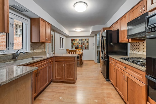 kitchen featuring sink, black appliances, light stone countertops, kitchen peninsula, and light wood-type flooring