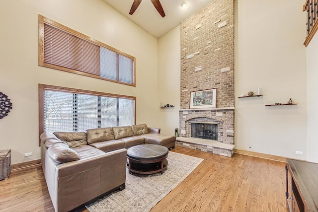 living room featuring a high ceiling, ceiling fan, a fireplace, and light hardwood / wood-style flooring