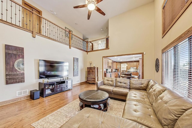 living room with ceiling fan, a towering ceiling, and light wood-type flooring