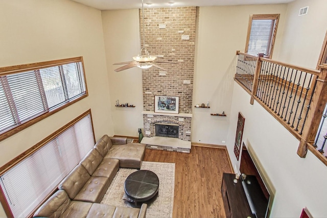 living room featuring ceiling fan, a towering ceiling, a fireplace, and light wood-type flooring