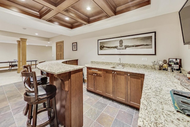 bar featuring coffered ceiling, sink, and light stone countertops