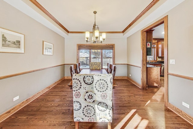 dining space featuring dark wood-type flooring, sink, a chandelier, ornamental molding, and a raised ceiling