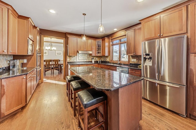 kitchen with pendant lighting, light hardwood / wood-style flooring, appliances with stainless steel finishes, a center island, and dark stone counters