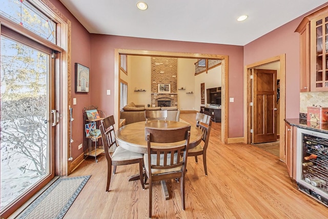 dining area with a brick fireplace, light hardwood / wood-style floors, and beverage cooler