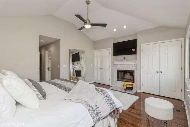 bedroom featuring multiple closets, a premium fireplace, lofted ceiling, and dark wood-type flooring