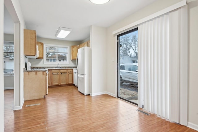 kitchen with light brown cabinetry, sink, light stone counters, light hardwood / wood-style flooring, and white appliances