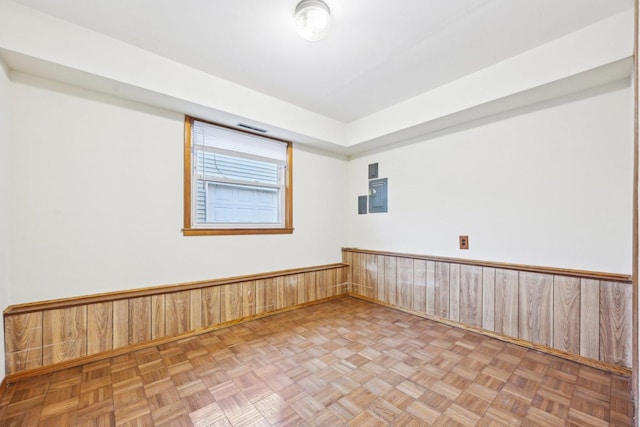 empty room with parquet flooring, electric panel, and wooden walls