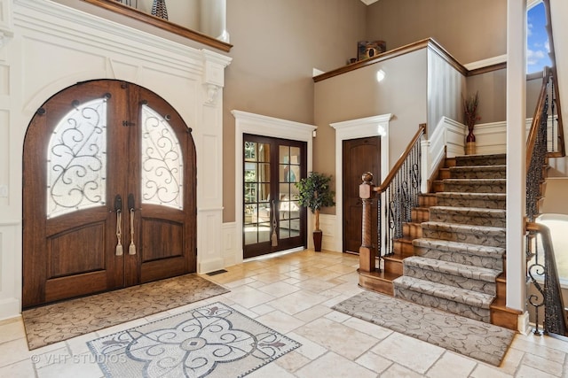 entryway with a towering ceiling, stairs, french doors, wainscoting, and stone tile flooring