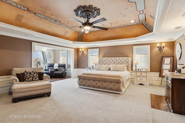 bedroom featuring light colored carpet, visible vents, ornamental molding, wainscoting, and a tray ceiling