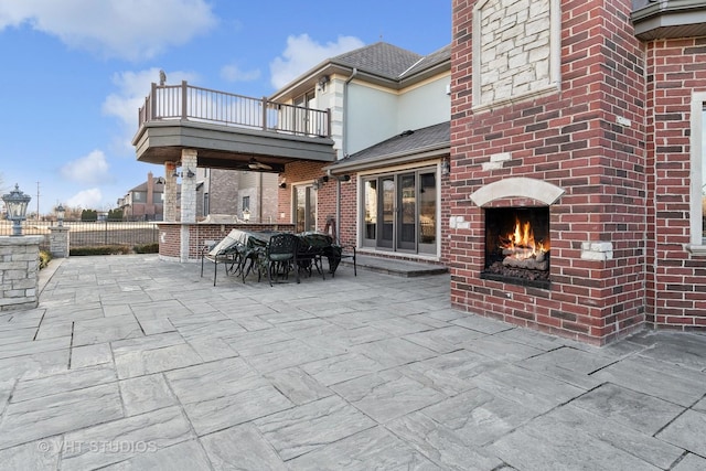 view of patio with an outdoor brick fireplace and a balcony