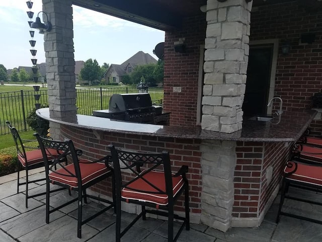 view of patio with fence, outdoor dry bar, a sink, and grilling area