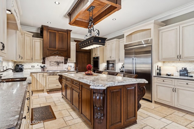 kitchen featuring stone tile flooring, hanging light fixtures, appliances with stainless steel finishes, a kitchen island, and a sink