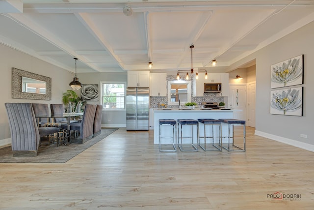 kitchen with stainless steel appliances, a breakfast bar, white cabinets, and decorative light fixtures