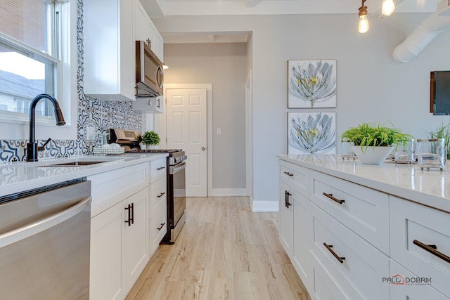 kitchen featuring sink, light hardwood / wood-style flooring, appliances with stainless steel finishes, decorative backsplash, and white cabinets