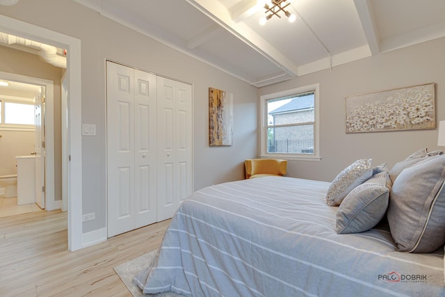 bedroom with a closet, light hardwood / wood-style flooring, and vaulted ceiling with beams