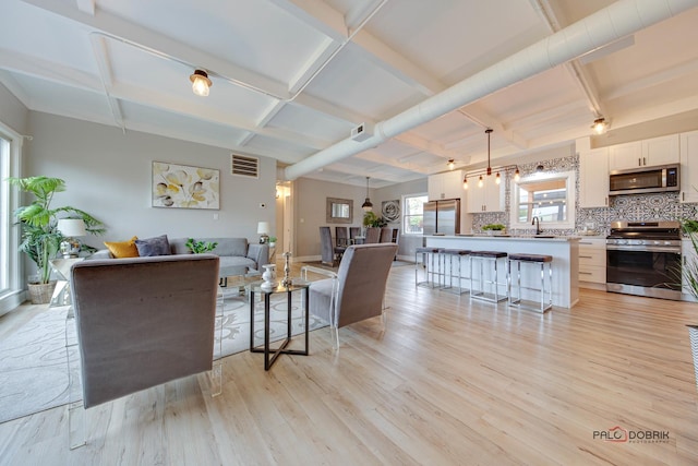 living room featuring coffered ceiling, sink, light hardwood / wood-style flooring, and beamed ceiling