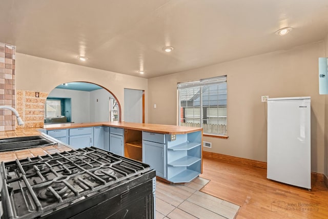 kitchen featuring wood counters, sink, tasteful backsplash, fridge, and light hardwood / wood-style floors