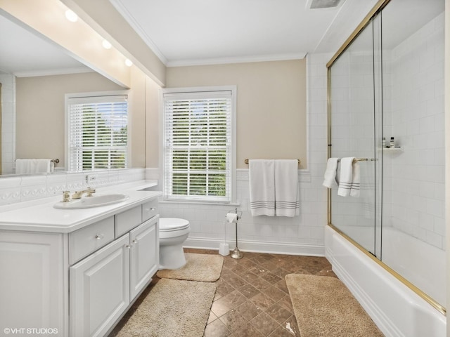 full bathroom featuring toilet, crown molding, bath / shower combo with glass door, tile walls, and vanity