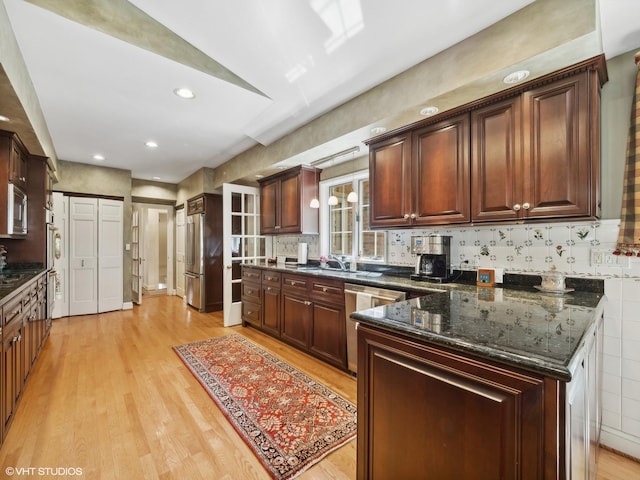 kitchen with sink, backsplash, stainless steel appliances, light hardwood / wood-style floors, and dark stone counters