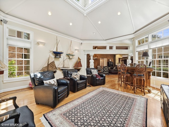living room with high vaulted ceiling, crown molding, decorative columns, and light wood-type flooring