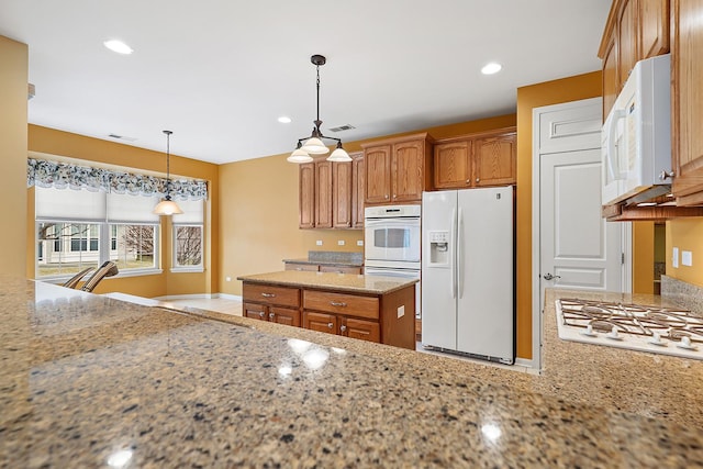 kitchen with a kitchen island, pendant lighting, light stone counters, and white appliances